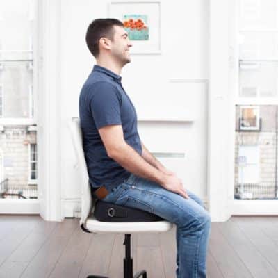 man sitting on black foundation (posture correction device)on white chair. Designed for back pain