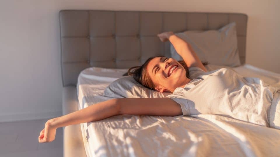 woman waking up in an orthopedic mattress to a warm sunrise
